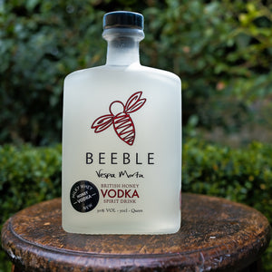 Bottle of Beeble Vespa Morta British Honey Vodka on a wooden surface with a green leafy background
